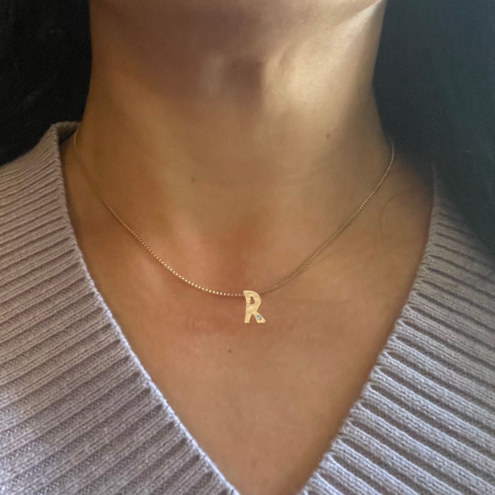 Gold diamond R necklace shown on woman's neck