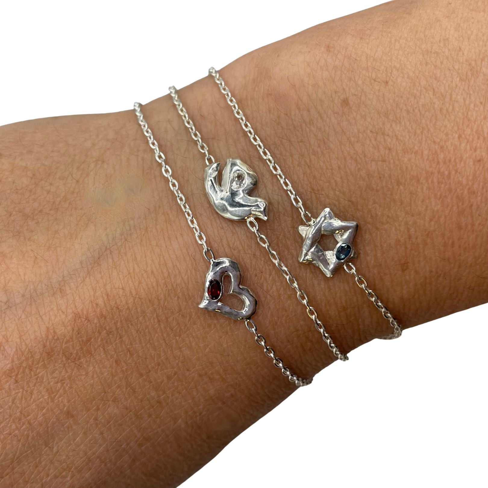 On wrist: Amy Delson sterling silver star, dove, and heart bracelets featuring London blue and white topaz and garnet gemstones