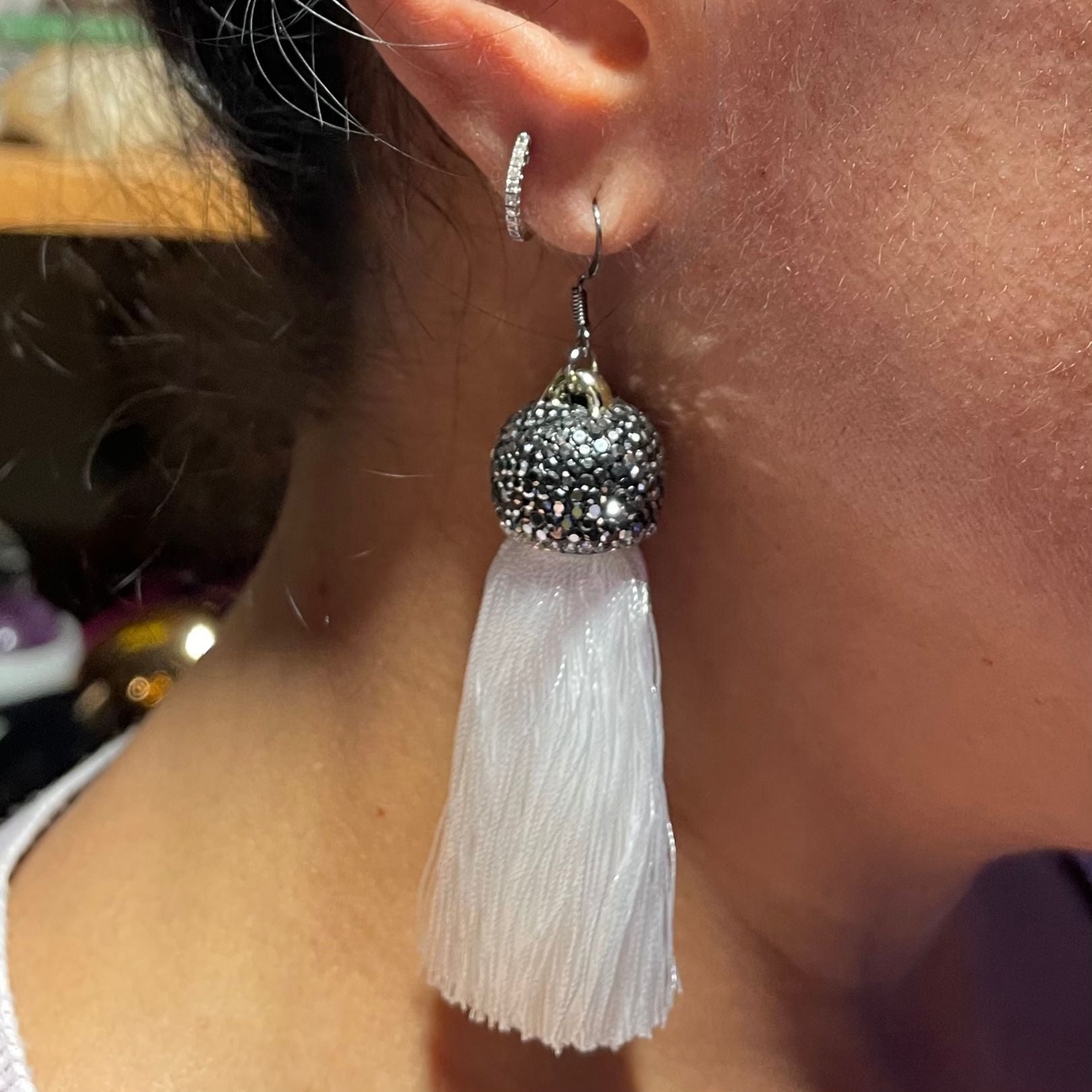 Amy Delson White Tassel earrings with crystals shown on an ear
